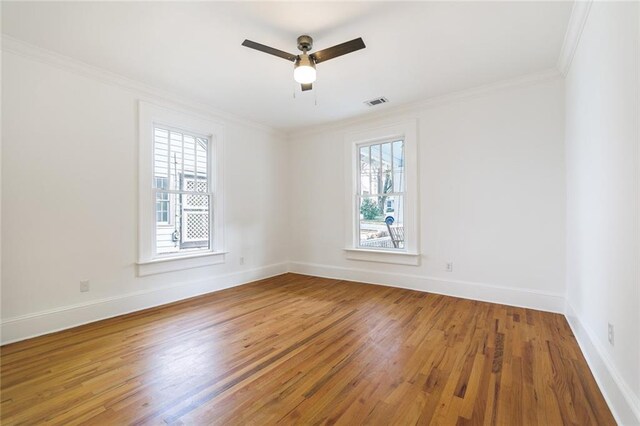 empty room featuring plenty of natural light, wood-type flooring, and ornamental molding