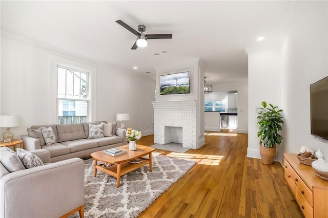 living room with ceiling fan, a fireplace, crown molding, and hardwood / wood-style flooring