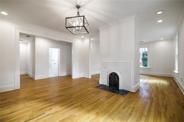 unfurnished living room with a tile fireplace, light wood-type flooring, a chandelier, and ornamental molding