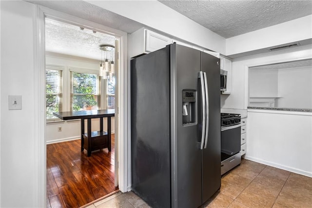 kitchen featuring baseboards, visible vents, stainless steel appliances, a textured ceiling, and white cabinetry