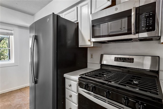 kitchen with light tile patterned floors, light countertops, appliances with stainless steel finishes, a textured ceiling, and white cabinetry