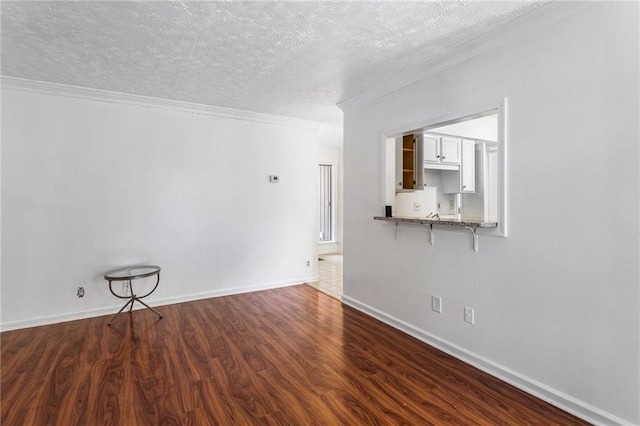 spare room with crown molding, wood finished floors, baseboards, and a textured ceiling