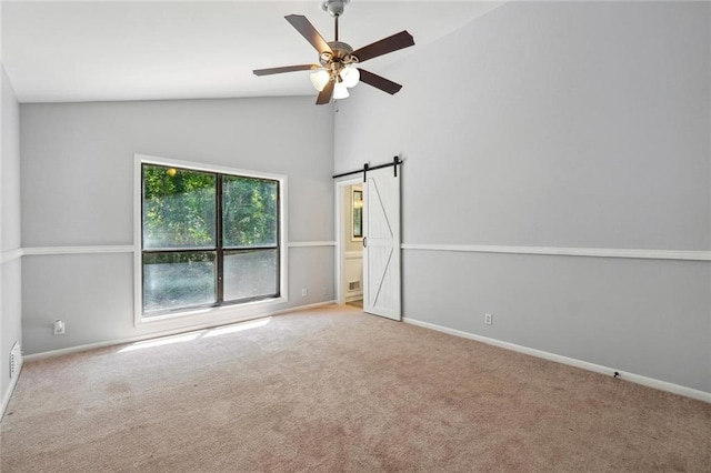 carpeted empty room featuring a barn door, ceiling fan, and vaulted ceiling