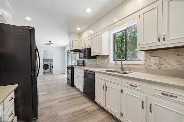 kitchen with sink, washing machine and dryer, light hardwood / wood-style floors, white cabinets, and black appliances