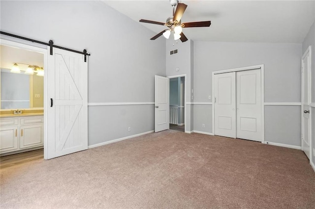 unfurnished bedroom featuring ceiling fan, a barn door, connected bathroom, light colored carpet, and a closet