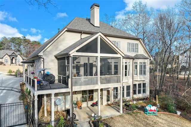 rear view of house featuring a patio area, a sunroom, a chimney, and roof with shingles