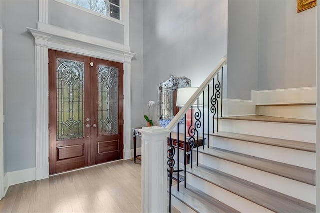 foyer entrance with wood finished floors, a healthy amount of sunlight, french doors, and a towering ceiling