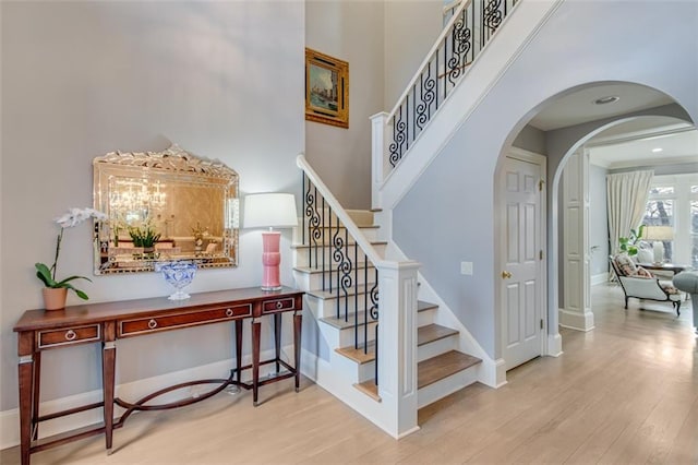 staircase with arched walkways, wood finished floors, a high ceiling, and baseboards