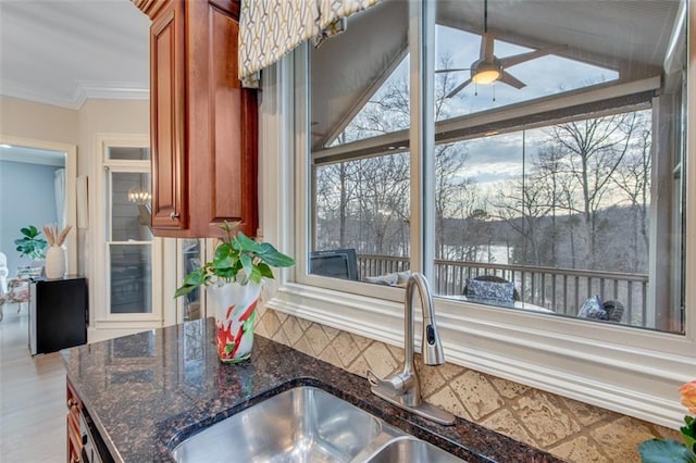 kitchen featuring dark stone countertops, wood finished floors, a ceiling fan, a sink, and brown cabinetry