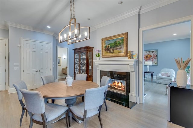 dining area with ornamental molding, a notable chandelier, a glass covered fireplace, and light wood finished floors