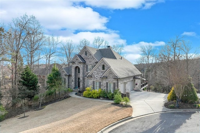 french provincial home with stone siding, a chimney, and concrete driveway
