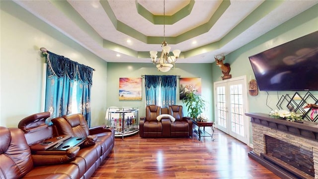 living room featuring a raised ceiling, wood-type flooring, an inviting chandelier, and french doors