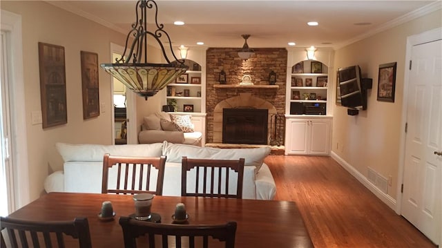 interior space with a stone fireplace, wood-type flooring, ornamental molding, and built in shelves