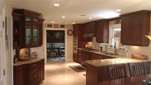 kitchen with stainless steel gas cooktop, sink, a breakfast bar, light stone counters, and kitchen peninsula