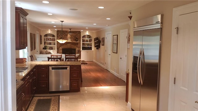 kitchen featuring built in features, stainless steel appliances, a stone fireplace, dark brown cabinetry, and hardwood / wood-style floors