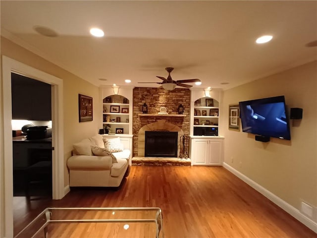 living room with built in shelves, hardwood / wood-style flooring, ceiling fan, and a stone fireplace