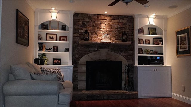 living room featuring hardwood / wood-style floors, a stone fireplace, built in shelves, and crown molding