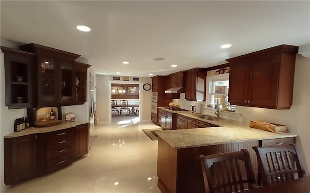 kitchen with stainless steel gas stovetop, light stone counters, kitchen peninsula, sink, and double oven