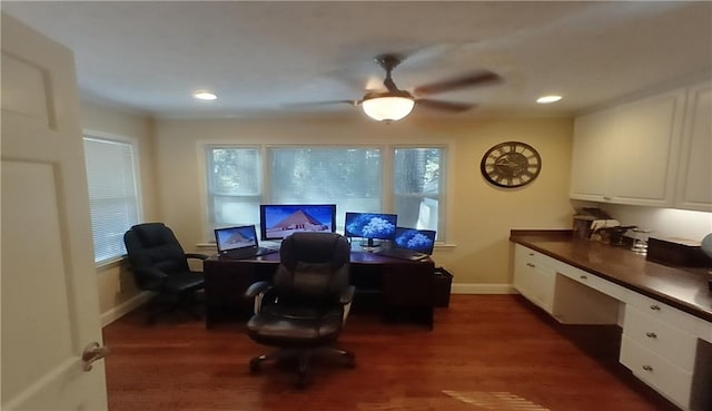 office featuring dark wood-type flooring, a wealth of natural light, built in desk, and ceiling fan