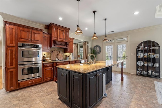 kitchen with a sink, light stone counters, decorative backsplash, appliances with stainless steel finishes, and a kitchen island with sink