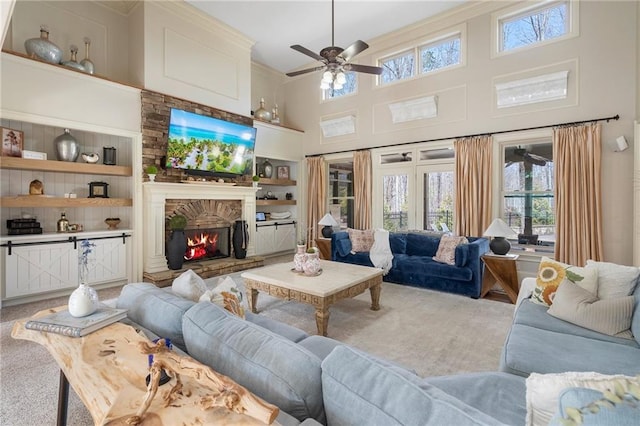 carpeted living area featuring built in shelves, ornamental molding, a high ceiling, a fireplace, and ceiling fan