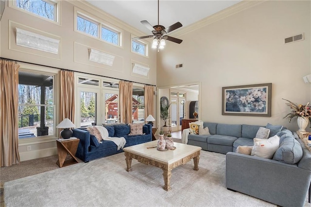 carpeted living room featuring visible vents, ceiling fan, crown molding, baseboards, and a towering ceiling