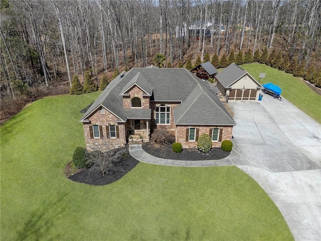 view of front of property featuring a wooded view, a front lawn, concrete driveway, a garage, and stone siding