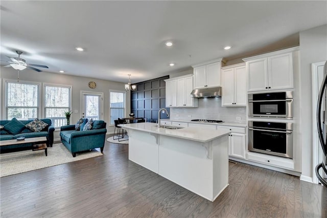 kitchen with open floor plan, a sink, under cabinet range hood, and backsplash