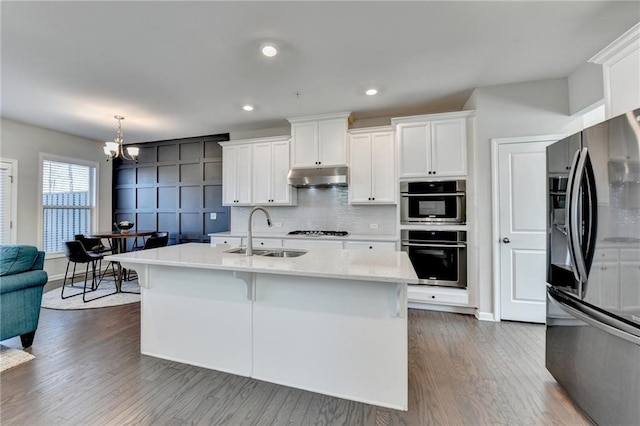 kitchen with stainless steel appliances, decorative backsplash, white cabinets, a sink, and under cabinet range hood