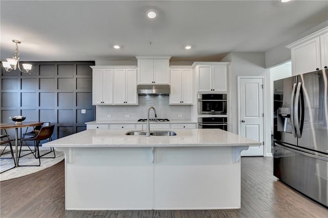 kitchen featuring under cabinet range hood, a sink, white cabinetry, appliances with stainless steel finishes, and tasteful backsplash