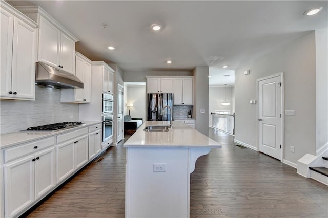 kitchen featuring dark wood finished floors, stainless steel appliances, under cabinet range hood, white cabinetry, and a sink