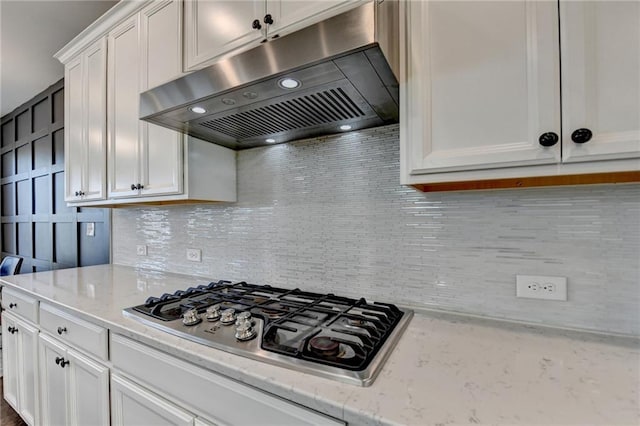 kitchen with tasteful backsplash, white cabinets, light stone counters, under cabinet range hood, and stainless steel gas stovetop