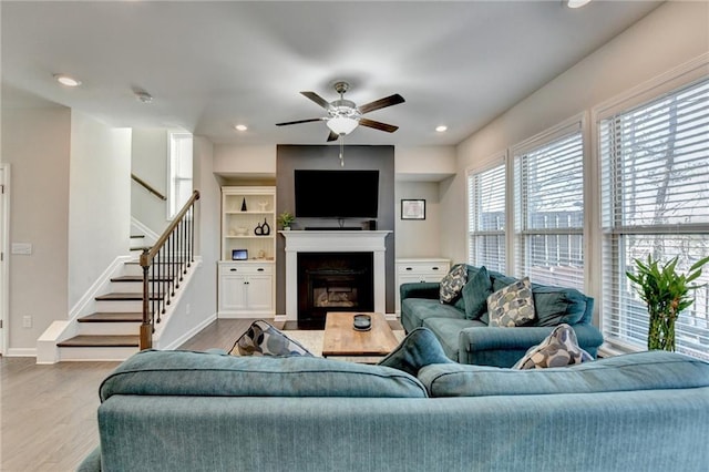 living area featuring a fireplace with flush hearth, wood finished floors, stairs, and baseboards