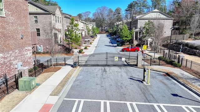 view of road with a gated entry, sidewalks, curbs, a gate, and a residential view