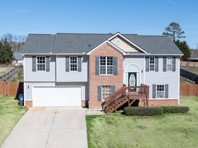 bi-level home featuring driveway, roof with shingles, an attached garage, fence, and a front lawn