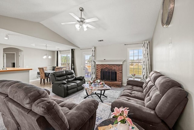 living room with visible vents, a brick fireplace, vaulted ceiling, baseboards, and ceiling fan with notable chandelier