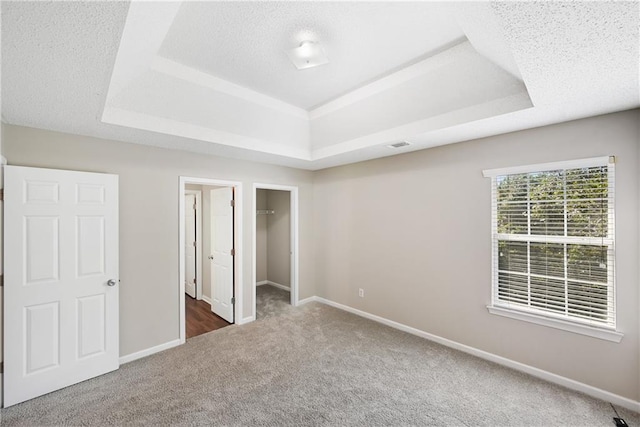 unfurnished bedroom with a spacious closet, a tray ceiling, a closet, and carpet floors