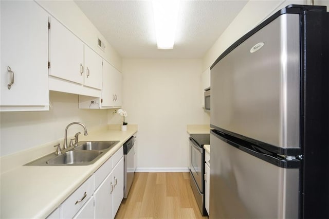 kitchen featuring sink, stainless steel appliances, a textured ceiling, white cabinets, and light wood-type flooring