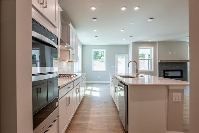 kitchen with sink, an island with sink, decorative backsplash, appliances with stainless steel finishes, and light wood-type flooring