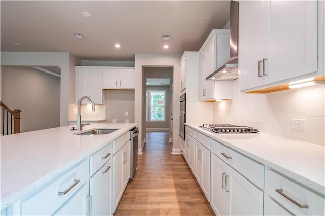 kitchen featuring appliances with stainless steel finishes, wall chimney range hood, sink, light hardwood / wood-style floors, and white cabinetry