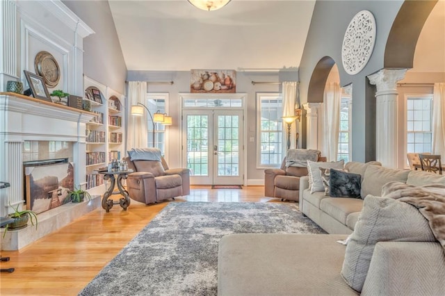 living room featuring lofted ceiling, french doors, decorative columns, a fireplace, and hardwood / wood-style floors