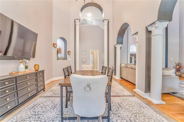 dining area with light hardwood / wood-style floors, ornate columns, and a high ceiling