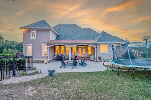 back house at dusk with a trampoline, a lawn, and a patio area