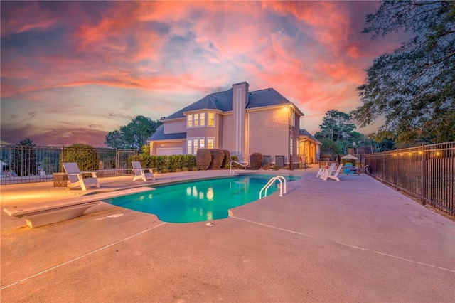 pool at dusk with a patio and a diving board