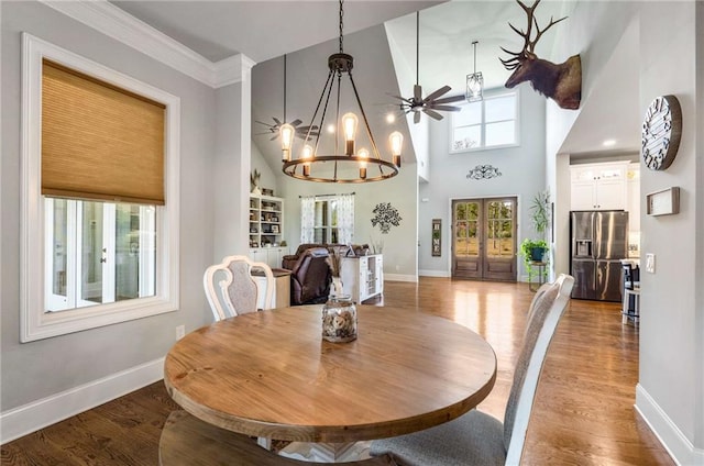 dining area with crown molding, a towering ceiling, wood-type flooring, and ceiling fan with notable chandelier