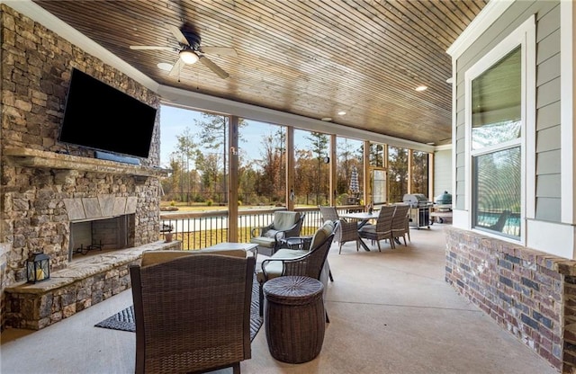 sunroom / solarium with ceiling fan, wood ceiling, and an outdoor stone fireplace