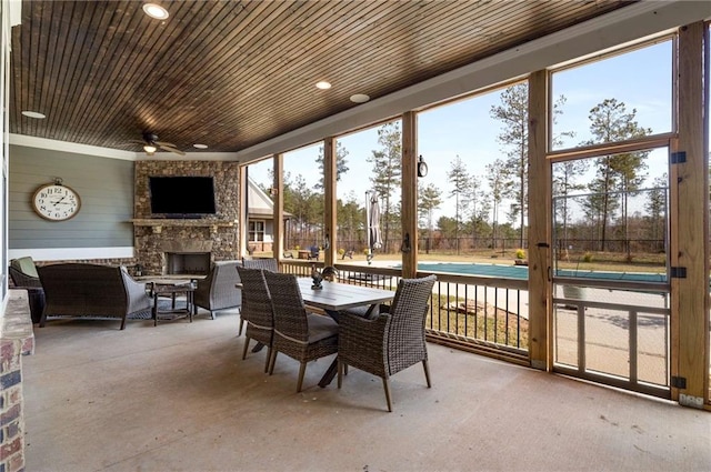 sunroom / solarium with a fireplace, ceiling fan, and wood ceiling