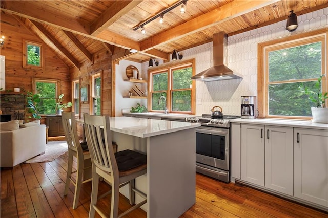 kitchen featuring wall chimney exhaust hood, stainless steel range oven, white cabinets, a center island, and light hardwood / wood-style floors