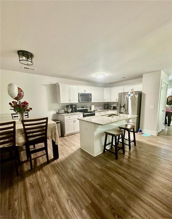 kitchen featuring a center island with sink, appliances with stainless steel finishes, white cabinets, light stone counters, and a breakfast bar