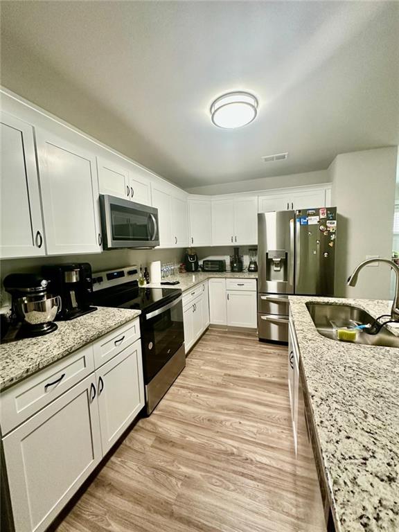 kitchen featuring appliances with stainless steel finishes, sink, light stone counters, and white cabinetry